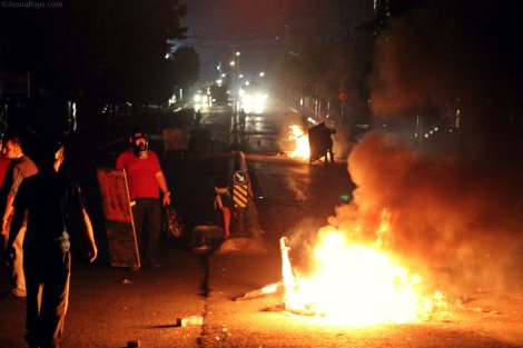 Protestors stand at the bottom of a hill, as water cannon trucks sit at the top of the hill before approaching the protestors to disperse them.