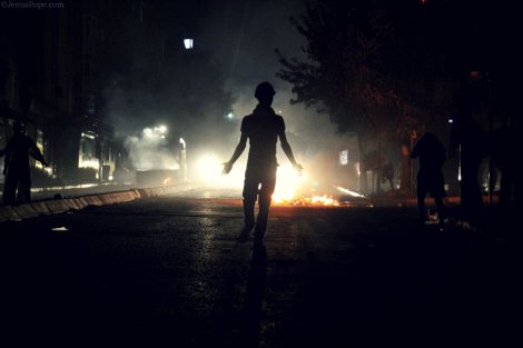 A protestor walks down the middle of the street as two water cannon trucks approach from behind.
