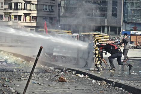 Protestors standing behind make-shift barricades as they are sprayed with a water cannon.