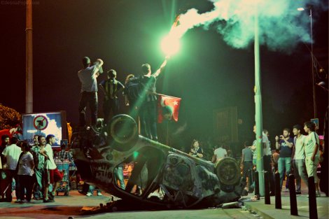 Protestors holding up a flare while standing on a destroyed car in Taksim Square.