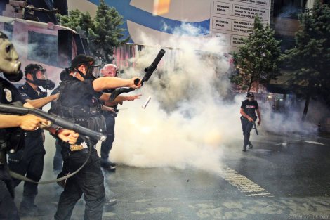 Police advancing towards protestors while shooting tear gas into the crowd on the street.